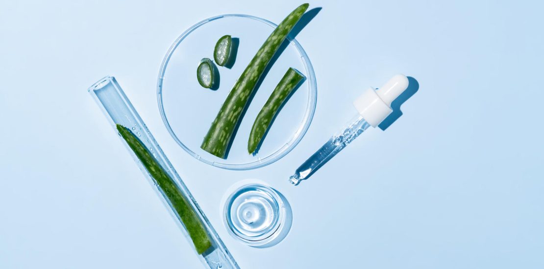 Aloe vera gel or extract with laboratory equipment, glassware. Organic green cosmetics, self care, beauty care concept on blue background with copy space